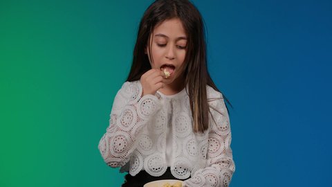 قضاء اوقات ممتعة باللعب ، تعابير الحيره والجهل بامر ما، استخدام التقنيات الحديثة للتسلية والترفيه، تصوير لبنت عربية خليجية اماراتيه مبتسمة ترتدي الزي الكاجوال تجلس على اريكة رمادية تقوم باللعب في ألعاب الفيديو بتعابير وايماءات الاندماج والتركيز، خلفية ملونه