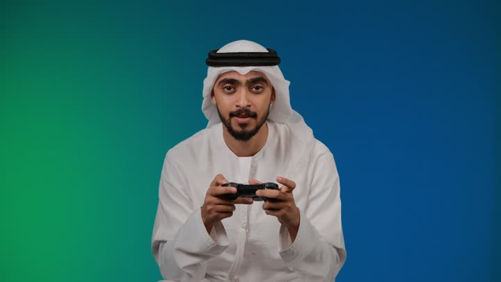Raising hand with loss gestures, interacting and merging with video games, having a fun and entertaining time, modern entertainment electronic devices and technologies, a picture of an Emirati Gulf Arab young man wearing a kandura and ghutra sitting on a comfortable chair and holding a joystick in his hand, a colorful background