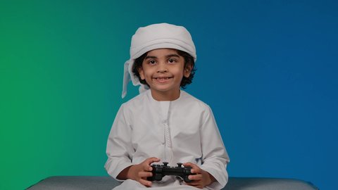 Enjoying modern technology and techniques, having a good time with video game consoles, the concept of fun and entertainment, entertainment computer programs, a close-up of a smiling Emirati Gulf Arab child holding a joystick, colorful background