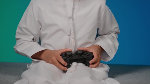 قضاء وقت ممتع بلعب ألعاب الفيديو، الاستمتاع بالتقنيات والتكنولوجيا الحديثة، مفهوم المتعة والتسلية، برامج الكمبيوتر الترفيهية، تصوير مقرب لطفل عربي خليجي اماراتى مبتسم  يمسك بيده عصا اللعب، خلفية ملونه