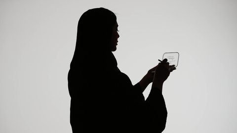 Marketing cosmetic products, using a cosmetic tool (eyeshadow brush), silhouette of an Arab Gulf Emirati woman wearing an abaya and hijab, interest in beauty and appearance, makeup tools tutorial, white background