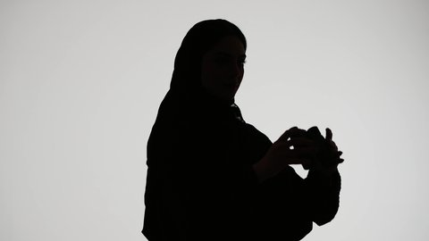 اتقان مهنه التصوير ،مصوره اماراتيه محترفه ، إلتقاط الصور التذكارية ، تصوير ظلي لامراه عربيه خليجيه اماراتيه ترتدي العباءه والحجاب، تحمل بيدها كاميرا تصوير عالية الدقة ،  خلفية بيضاء
