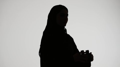 إلتقاط الصور التذكارية ، تصوير ظلي لامراه عربيه خليجيه اماراتيه ترتدي العباءه والحجاب، تحمل بيدها كاميرا تصوير عالية الدقة ، مصوره اماراتيه محترفه ، اتقان مهنه التصوير ، خلفية بيضاء