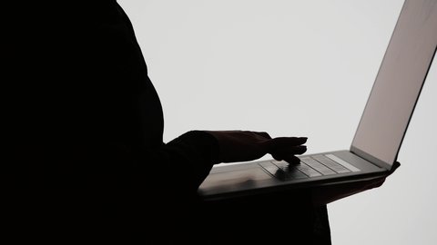 Social media, use of modern technology devices, completing work tasks using a laptop, integrating modern technology into daily life, making a video call, silhouette of an Arab Gulf Emirati woman wearing an abaya and hijab holding a laptop, white background