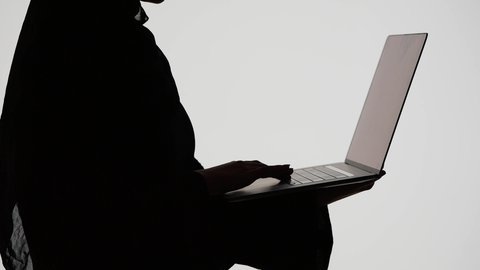 إستخدام اجهزة تقنية حديثة ،انجاز مهام العمل بإستخدام الحاسوب المحمول، دمج التكنولوجيا الحديثه فى الحياه اليوميه ، اجراء مكالمه فيديو ، وسائل التواصل الإجتماعي ، تصوير ظلي لمرأة عربية خليجية اماراتيه ترتدي العباءه والحجاب تمسك بيدها جهاز اللابتوب ، خلفية بيضاء