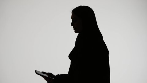 Live broadcast, using modern technology, taking commemorative selfies with a mobile phone, making a phone call, silhouette of an Emirati Gulf Arab woman wearing an abaya and hijab, social media, white background