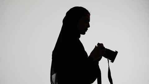 Memorial photo shoot, silhouette of an Arab Gulf Emirati woman wearing an abaya and hijab, holding a high-resolution camera, professional Emirati photographer, photography proficiency, white background