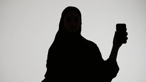 عرض شاشة سوداء فارغه، استخدام التكنولوجيا الحديثه، تصوير ظلي لمرأة عربية خليجية اماراتيه ترتدي العباءه والحجاب ، تعرض بيدها شاشه الجوال ، عرض البرامج والتطبيقات ، خلفية بيضاء