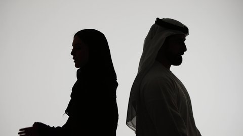 تصوير ظلي لزوجان عربيان خليجيان اماراتي، يقفان بإستقامة وإيدي متقاطعة ، ينظران إلى الجانب ، مفهوم الاناقه والاهتمام بالمظهر الخارجي ،الالفه والموده بين الازواج، خلفية بيضاء