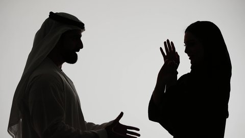مشاكل عائلية وصراع اسري، ازمة في العلاقات الاسرية، دفاع المرأة عن نفسها،  شجار بين الزوجين،رجل إماراتي يرتدي الغترة والكندورة يقوم بضرب وتعنيف زوجته على وجهها، تصوير ظلي لزوجين عربيين خليجيين اماراتيين يتجادلان مع بعضهما بإيماءات الغضب، خلفية بيضاء