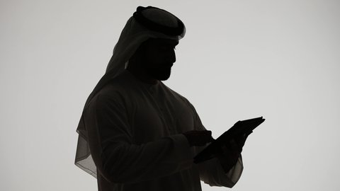 Completing tasks remotely, integrating modern technologies into daily life, shopping via online applications using a tablet, online chatting, Emirati jobs and professions, communicating with family and friends, silhouette of an Emirati Gulf Arab man holding a laptop, white background