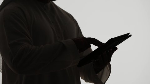 Integrating modern technologies into daily life, shopping via online applications using a tablet, online chatting, Emirati jobs and professions, communicating with family and friends, completing tasks remotely, silhouette of an Emirati Gulf Arab man holding a laptop, white background