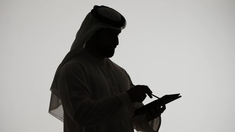 Online shopping using tablets, online chatting, Emirati jobs and professions, integrating modern technologies into daily life, communicating with family and friends, completing tasks remotely, silhouette of an Emirati Gulf Arab man holding a laptop, white background
