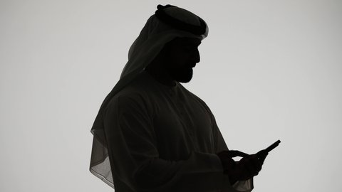الدردشه عبر الانترنت، دمج التقنيات الحديثه فى الحياه اليوميه ، إجراء مكالمة فيديو بإستخدام الهاتف المحمول ، ادارة الاعمال وتحقيق الأهداف أونلاين، إنجاز المهام عن بعد، تصوير ظلي لرجل عربي خليجي اماراتي يمسك بيده الجوال ، خلفية بيضاء