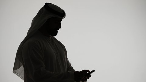 Business management and achieving goals online, making a video call using a mobile phone, online chatting, integrating modern technologies into daily life, completing tasks remotely, silhouette of an Emirati Gulf Arab man holding a mobile phone, white background