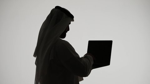 إستخدام جهاز الحاسوب المحمول ، تصفح مواقع التواصل الاجتماعي ، دمج التقنيات الحديثه فى الحياه اليوميه ، تصوير ظلي لرجل عربي خليجي اماراتي ،إستخدام اجهزة تكنولوجيا حديثة ، العمل عن بعد ، مفهوم التسويق الإلكتروني ، مهن ووظائف اماراتيه ، خلفية بيضاء