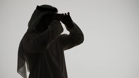 A love of exploration and adventure, seeing distant things and bringing them closer. A silhouette of an Arab Gulf Emirati man holding binoculars and looking at something with gestures of pleasure and enjoyment, white background.