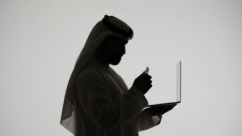 Online shopping and ordering, paying by credit card, using a laptop, silhouette of an Arab Gulf Emirati man, using modern technology devices, remote work, the concept of e-marketing, Emirati professions and jobs, white background