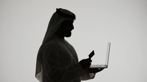 Credit card payment, online shopping and ordering, using a laptop, silhouette of an Arab Gulf Emirati man, using modern technology, remote work, the concept of e-marketing, Emirati professions and jobs, white background