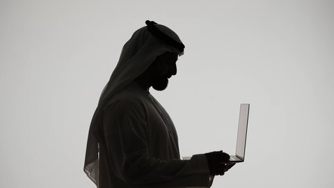 إستخدام جهاز الحاسوب المحمول ، تصفح مواقع التواصل الاجتماعي ، تصوير ظلي لرجل عربي خليجي اماراتي ، إستخدام اجهزة تقنية حديثة ، العمل عن بعد ،مفهوم التسويق الإلكتروني ، مهن ووظائف اماراتيه ، خلفية بيضاء