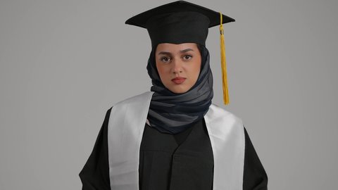 مفهوم الحيره ، تعابير الجهل وعدم معرفه شئ ما ، إنهاء الدراسة الجامعية، تحقيق حلم النجاح, الاحتفال بالتخرج من الجامعة، مفهوم الاجتهاد والتفوق ، بورترية مقرب لطالبة عربية خليجية اماراتيه محجبة ترتدي روب التخرج والقبعة، خلفية رمادية