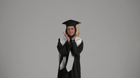 المناسبات والاحتفالات الجامعية,بورتريه طالبة جامعية خريجة عربية اماراتية خليجية تلبس قبعة التخرج , ايماءات وجه ويدين تدل على السعادة بالتفوق والنجاح, تلميذه متفوقه, مدارس وجامعات, التعليم في الامارات العربية , خلفية رمادية