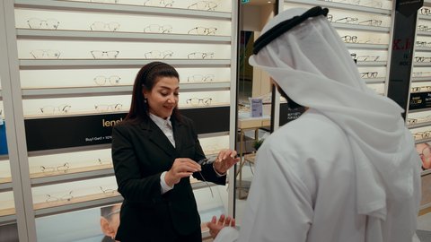 سيده اماراتيه تقوم بمساعده الزبائن في اختيارمقاسات النظارات المناسبه لهم، رجل اماراتي يرتدي الكندوره والغتره البيضاء يقوم باختيار النظارة الطبيه المناسبة، الاهتمام بالمظهر الخارجي، التسوق وشراء النظارات الطبيه من المولات