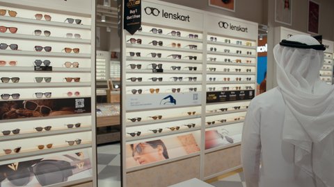 شاب اماراتي يرتدي الكندوره والغتره البيضاء يقوم بالنظر الي المرآه لقياس النظارة الشمسيه المناسبة، الاهتمام بالمظهر الخارجي، التسوق وشراء النظارات الشمسيه من المولات، عروض وتخفيضات، ايماءات الثقة بالنفس