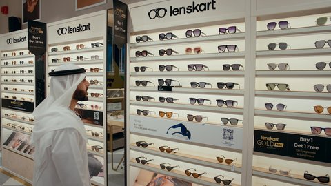 Trying on black sunglasses before buying, the joy of shopping and buying by choosing suitable sunglasses, an Arab Gulf Emirati man wearing a kandura trying on sunglasses, confusion in choosing suitable glasses, interest in the external appearance