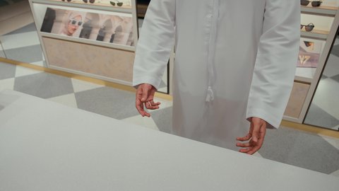 متعة التسويق والشراء باختيار نظارة شمسية مناسبة، تصوير مقرب ليدين رجل عربي خليجي اماراتي يرتدي الكندوره يقوم بفتح خزانه مليئه بالنظارات الشمسيه، قضاء وقت ممتع، الحيرة في اختيار نظارة مناسبة