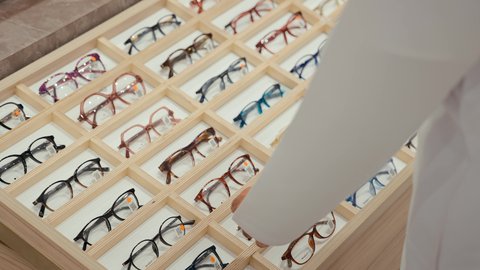 نظارات طبيه كثيره ملونه ومتنوعه، متعة التسويق والشراء باختيار نظارة طبيه مناسبة، تصوير مقرب ليدين رجل عربي خليجي اماراتي يرتدي الكندوره يقوم باختيار نظاره طبيعه، الحيرة في اختيار نظارة مناسبة