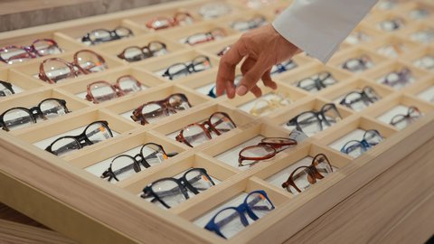 فحص النظارات الطبيه الملونه قبل الشراء، متعة التسويق والشراء باختيار نظارة طبيه مناسبة، تصوير مقرب ليدين رجل عربي خليجي اماراتي يرتدي الكندوره يقوم باختيار نظاره طبيعه، الحيرة في اختيار نظارة مناسبة