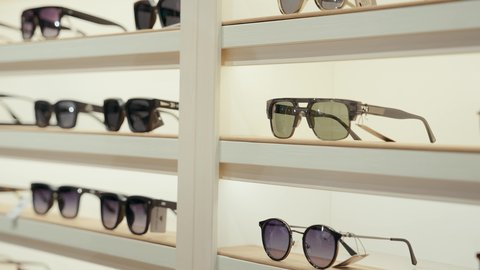 ارفف عرض النظارات داخل المحل، انواع وماركات النظارات الشمسيه العالميه، القيام ارتداء النظارات الشمسيه قبل الشراء، متعة التسويق والشراء باختيار نظارة شمسيه مناسبة،  رجل عربي خليجي اماراتي يرتدي الكندوره يقوم بقياس نظاره سوداء، الاهتمام بالمنظر الخارجي