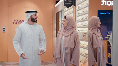 سيده اماراتيه ترتدي عباءه ورديه تستمتع باختيار وقياس نظارة طبيه مناسبة برفقه زوجها،  رجل عربي خليجي اماراتي يرتدي الكندوره يقوم باختيار نظاره طبيه لزوجته، ارفف عرض النظارات، انواع وماركات النظارات الطبيه، تحسين الرؤيه والنظر