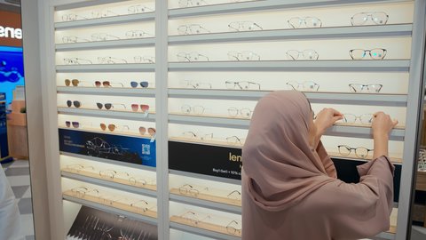 الاختيار الامثل للنظارات الطبيه، سيده اماراتيه ترتدي عباءه ورديه تستمتع باختيار وقياس نظارة طبيه مناسبة برفقه زوجها،  رجل عربي خليجي اماراتي يرتدي الكندوره يقوم باختيار نظاره طبيه لزوجته، ارفف عرض النظارات، تحسين الرؤيه والنظر