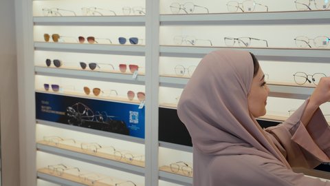 الاختيار الامثل للنظارات الطبيه، سيده اماراتيه ترتدي عباءه ورديه تستمتع باختيار وقياس نظارة طبيه مناسبة برفقه زوجها،  رجل عربي خليجي اماراتي يرتدي الكندوره يقوم باختيار نظاره طبيه لزوجته، ارفف عرض النظارات، تحسين الرؤيه والنظر