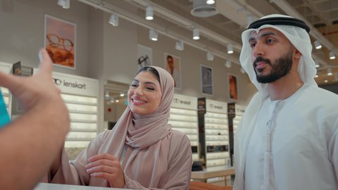متابعة آخر صيحات الموضة والجمال, تسوق وشراء أحدث منتجات النظارات العصرية الحديثة, زوجان عربيان خليجيان اماراتيان في متجر النظارات الشمسيه, رجل اماراتي يقوم بالدفع الالكتروني برفقه زوجته، تطبيقات الهاتف للدفع عبر الانترنت، استخدام الاجهزه الحديثه