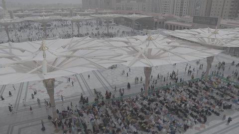 A religious landmark and a sacred Islamic place during the day, pilgrims and Umrah performers gather in the outer courtyard of the Prophet's Mosque in Medina, Saudi Arabia, modern electronic umbrellas, the architectural art of the minarets and the Green Dome