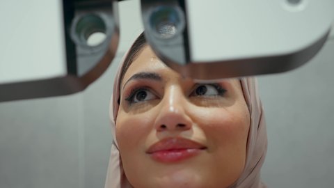 استخدام الأجهزة الحديثة المتطورة، تقييم الرؤية والكشف عن أمراض العيون للمريض،تصوير مقرب لامراة عربيه خليجيه اماراتية ترتدي العباءه الملونه في عيادة مختصة لفحص العيون تنظر من خلال مجموعة من العدسات ،مفهوم الخدمات والرعاية الصحية في المستشفيات والمراكز، الزيارة الدورية للعيادات العينية في الامارات