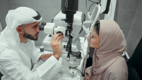 استخدام الأجهزة الحديثة المتطورة، مفهوم الخدمات والرعاية الصحية في المشافي والمراكز الطبية، تشخيص وتحديد المشاكل البصرية، تصوير مقرب من الجانب لطبيب عربي خليجي اماراتي يقوم بفحص عينى امراه  اماراتية بجهاز المنظار العيني، تقييم مدى الرؤية والكشف عن الامراض العينية