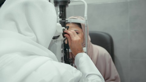 The concept of healthcare services in hospitals and medical centers, the use of modern, advanced equipment, diagnosis and identification of visual problems, a close-up of an Emirati Gulf Arab doctor examining the eyes of an Emirati woman with an ophthalmoscope, assessing vision and detecting eye diseases.
