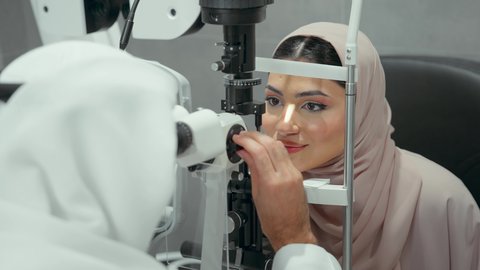 Using modern, advanced equipment, diagnosing and identifying visual problems, a close-up of an Emirati Gulf Arab doctor examining the eyes of an Emirati woman with an ophthalmoscope, assessing vision and detecting eye diseases, the concept of services and healthcare in hospitals and medical centers.