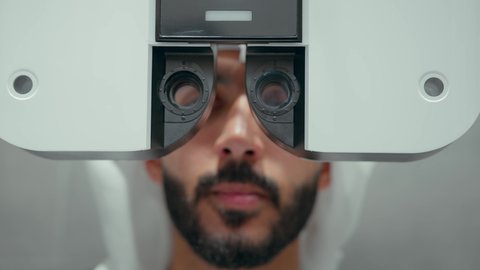 تقييم الرؤية والكشف عن أمراض العيون للمريض،تصوير مقرب لرجل عربي خليجي اماراتي يرتدي الزي التقليدي في عيادة مختصة لفحص العيون ينظر من خلال مجموعة من العدسات ،مفهوم الخدمات والرعاية الصحية في المستشفيات والمراكز، استخدام الأجهزة الحديثة المتطورة، الزيارة الدورية للعيادات العينية في الامارات