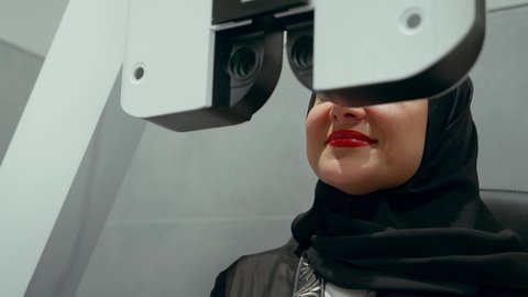 تقييم مدى الرؤية والكشف عن الامراض العينية، مفهوم الخدمات والرعاية الصحية في المستشفيات والمراكز، استخدام الأجهزة الحديثة المتطورة، تشخيص وتحديد المشاكل البصرية، تصوير مقرب لامراة عربية خليجية اماراتية ترتدي العباءة امام جهاز فحص العين للتأكد من صحة البصر