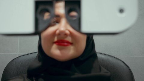تقييم مدى الرؤية والكشف عن الامراض العينية، استخدام الأجهزة الحديثة المتطورة، تشخيص وتحديد المشاكل البصرية، تصوير مقرب لامراة عربية خليجية اماراتية ترتدي العباءة امام جهاز فحص العين للتأكد من صحة البصر، مفهوم الخدمات والرعاية الصحية في المستشفيات والمراكز