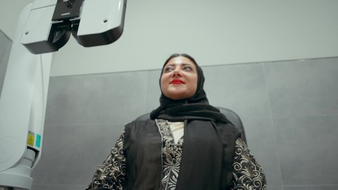 استخدام الأجهزة الحديثة المتطورة، تشخيص وتحديد المشاكل البصرية، تصوير مقربة لامراة عربية خليجية اماراتية ترتدي العباءة امام جهاز فحص العين للتأكد من صحة البصر، تقييم مدى الرؤية والكشف عن الامراض العينية، مفهوم الخدمات والرعاية الصحية في المستشفيات والمراكز