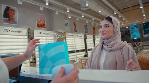 تحسين الرؤية ومحاولة تعديل البصر، امراه عربيه خليجيه اماراتية محجبه ترتدي العباءه الملونه تقوم بشراء النظارة الطبيه المناسبة في محل نظارات تحملها في كيس ورقي ملون، الاهتمام بالمظهر الخارجي، شراء النظارات الخاصة بضعف النظر، التسوق وشراء النظارات الطبيه