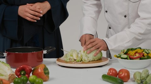 مفهوم النظام الغذائي، سلطة الخضار الطازجة اللذيذة، الاستمتاع بالعمل الجماعي في مهنة الطبخ، أدوات خاصة بالمطبخ، تعلم وتطبيق فنون الطهي، تصوير مقرب ليد رجل وامرأة عربيين خليجيين اماراتيان يتشاركان في تجهيز الطعام، رجل خليجي يقوم  بتقطيع الخس لاعداد السلطه
