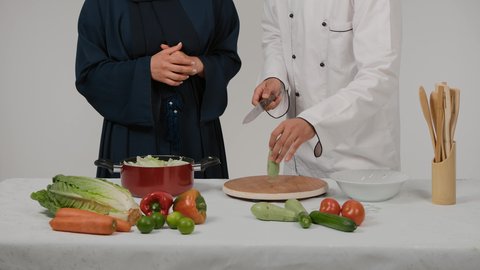 الاستمتاع بالعمل الجماعي في مهنة الطبخ، أدوات خاصة بالمطبخ، تعلم وتطبيق فنون الطهي، تصوير مقرب ليد رجل وامرأة عربيين خليجيين اماراتيان يتشاركان في تجهيز الطعام، رجل خليجي يقوم بتقطيع الكوسة