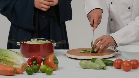 اعداد السلطة والأطباق الصحية، تعلم وتطبيق فنون الطهي، المشاركة في تحضير الوصفات الشهية، تصوير مقرب ليد رجل وامرأة عربيين خليجيين اماراتيان يتشاركان في تجهيز الطعام، رجل خليجي يقوم بتقطيع الخيارلاعداد السلطة
